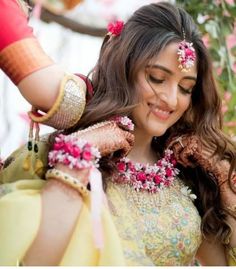 a woman in a yellow and pink outfit with flowers on her head is smiling at the camera