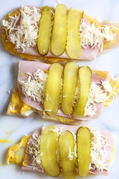 three hot dogs with ham, cheese and pickle slices on them sitting on a marble surface