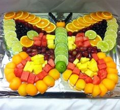 a butterfly made out of fruit on top of a sheet of tin foil with limes, oranges, grapes and watermelon