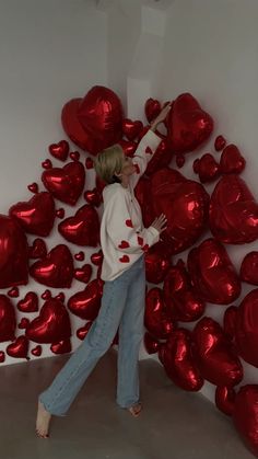 a woman standing in front of a wall with red heart balloons on it's sides