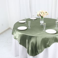 a green table cloth with white plates and vases on it, set up for a formal function