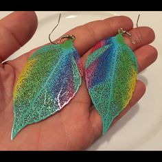 a hand holding two colorful leaf shaped earrings