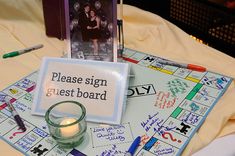 a game board with a candle and some writing on it, next to a card that says please sign guest board