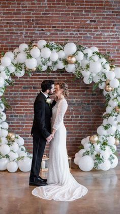 a bride and groom standing in front of a large balloon arch with white balloons on it