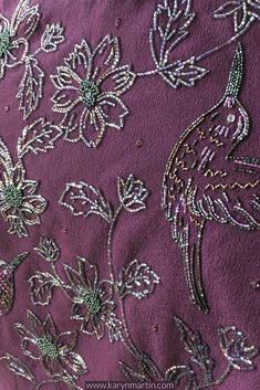 an embroidered fabric with flowers and birds on purple background, close - up view from the neck down