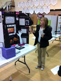 a woman standing in front of a table with posters on it and people looking at them