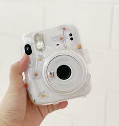 a person holding up a camera in front of a white wall with flowers on it