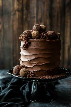 a chocolate cake with frosting and nuts is on a black platter against a wooden background