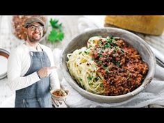 a man standing in front of a bowl of spaghetti and meat sauce on a table