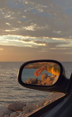 a person's hand is reflected in the side view mirror of a car near the ocean