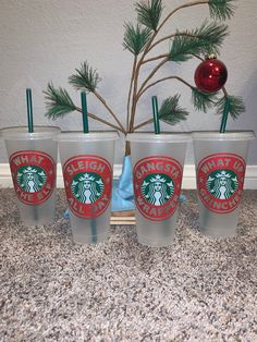 four starbucks cups sitting on top of a counter next to a christmas tree and a red ornament