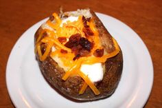 a baked potato with cheese and bacon on it sitting on a white plate next to a wooden table