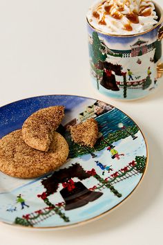 two cookies on a plate next to a cup of hot chocolate and marshmallows