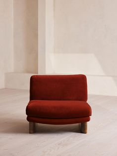 a red couch sitting on top of a hard wood floor next to a white wall