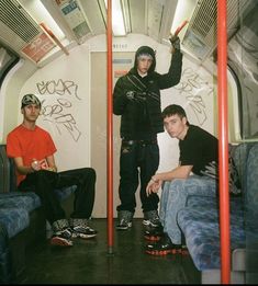 three men sitting in a train car with graffiti on the walls and one standing up