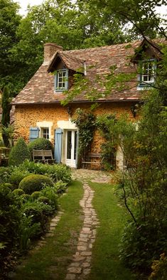 a stone house with blue shutters and windows in the front yard is surrounded by greenery