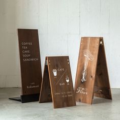 three wooden signs sitting next to each other on top of a cement floor in front of a white wall