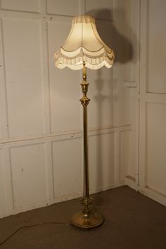 a floor lamp with a white shade on it's base in front of a wall