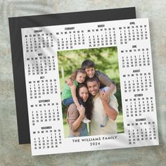 a family photo calendar on a table next to a black and white wall hanging from a metal frame