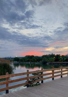 a wooden bridge over a body of water under a sky filled with clouds at sunset