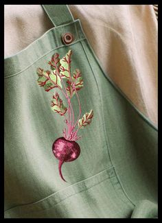 an embroidered radish on the back of a green apron with pink thread work