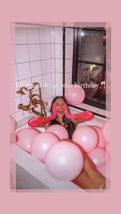 a woman laying in a bathtub filled with pink balloons