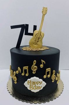 a black and gold birthday cake with musical notes on top, guitar in the middle