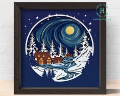 a framed paper cut art depicting a snowy night with houses and trees in the snow