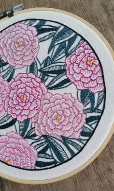 a close up of a embroidery on a wooden surface with pink flowers in the center