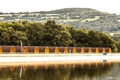 a row of orange benches sitting on top of a lake next to a lush green hillside