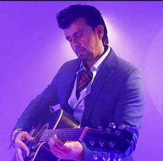 a man wearing a suit and tie playing an acoustic guitar in front of a purple background