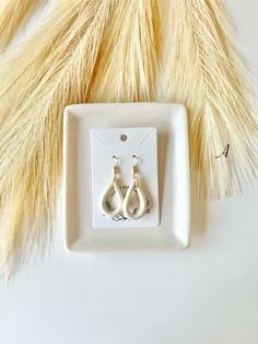 two pairs of earrings sitting on top of a white plate next to a yellow feather