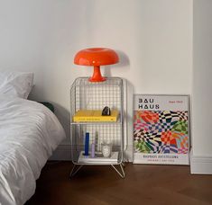 an orange lamp is next to a bed with white sheets and a poster on the wall