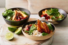 two bowls filled with food on top of a wooden table next to lime wedges