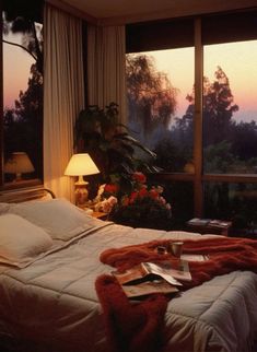 a bed sitting next to a window in a bedroom under a blanket and two lamps