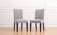 two gray chairs sitting side by side in front of a white wall and wooden floor