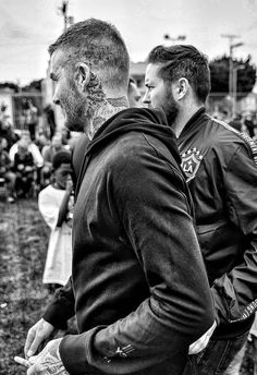 two men standing next to each other in front of a group of people with tattoos on their faces