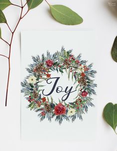 a christmas card with the word joy surrounded by greenery and leaves on a white background