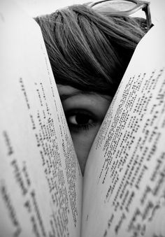 an image of a person peeking out from behind two books with their faces hidden in the pages