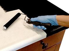 a person in blue gloves is cleaning a white counter top with a black brush and knife