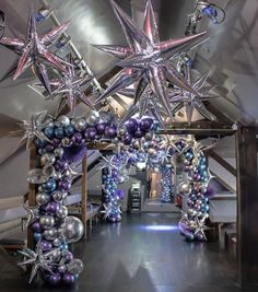 an archway decorated with silver and purple balloons, star shaped decorations and hanging from the ceiling