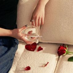 a woman is sitting on a couch with rose petals around her and holding a glass bowl