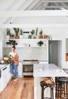 a woman standing in a kitchen next to an oven and counter top with potted plants on it