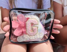 a girl is holding a clear bag with pink and white decorations on the bottom, which reads g