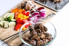 chopped vegetables and meat in a bowl on a wooden cutting board next to a metal tray