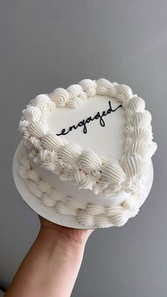 a hand holding a white cake with the word engaged written on it in cursive writing