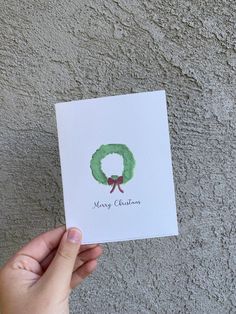 someone holding up a christmas card with a green wreath on it