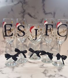 four wine glasses with black bows and santa hats on them sitting on a marble counter top