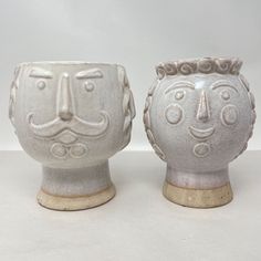 two white vases with faces on them sitting next to each other in front of a white background