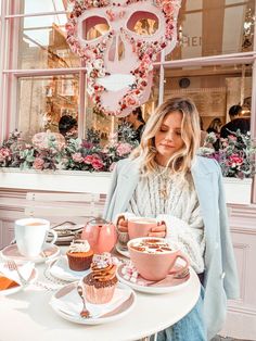 a woman sitting at a table with cupcakes and coffee